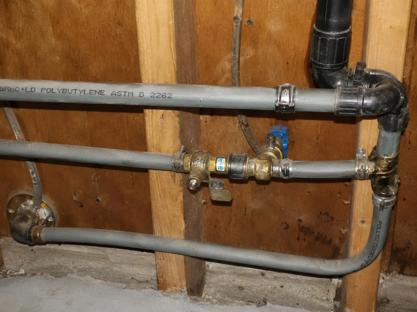 Gray polybutylene supply pipes stamped POLYBUTYLENE ASTM D 2262 inside the wall of a home