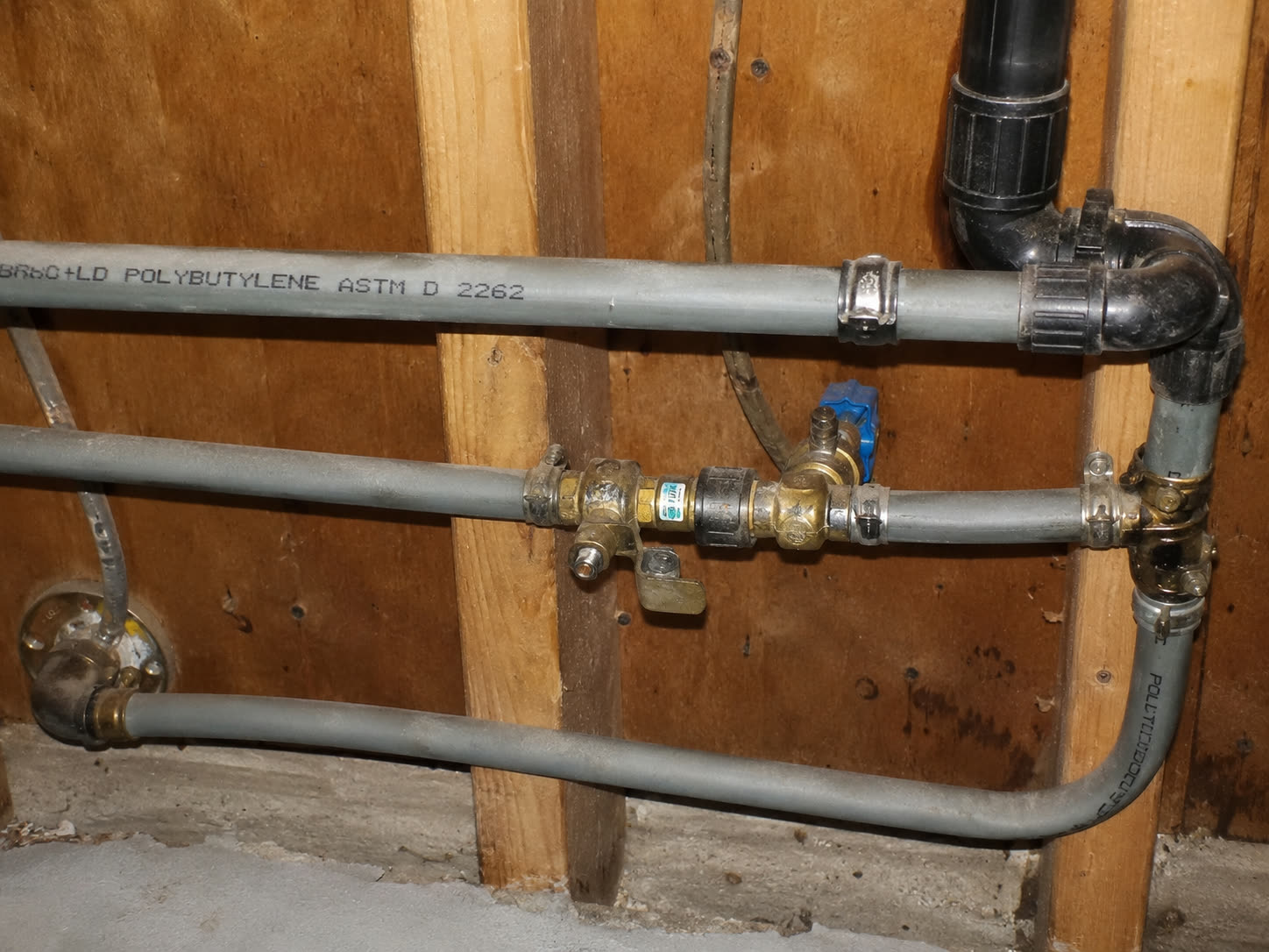 Gray polybutylene supply pipes stamped POLYBUTYLENE ASTM D 2262 inside the wall of a home
